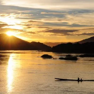 Une pirogue passe sur le Mékong sous un coucher de soleil lumineux
