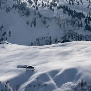 Paysage hivernal vu d'en haut, des chalets parsèment l'immensité blanche, deux silhouettes marchent au loin dans les Alpes